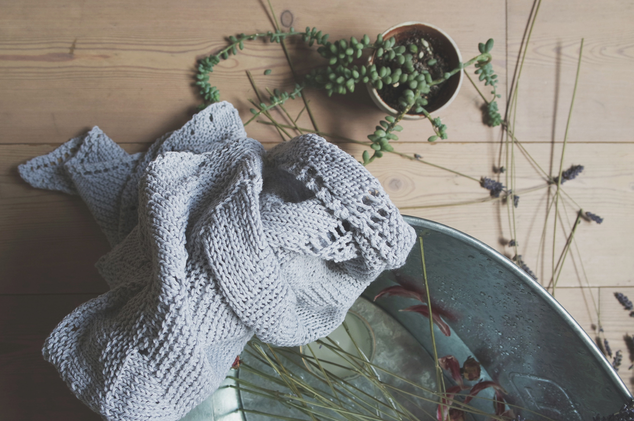 Gebreide babykleding met groene takjes in een metalen mand