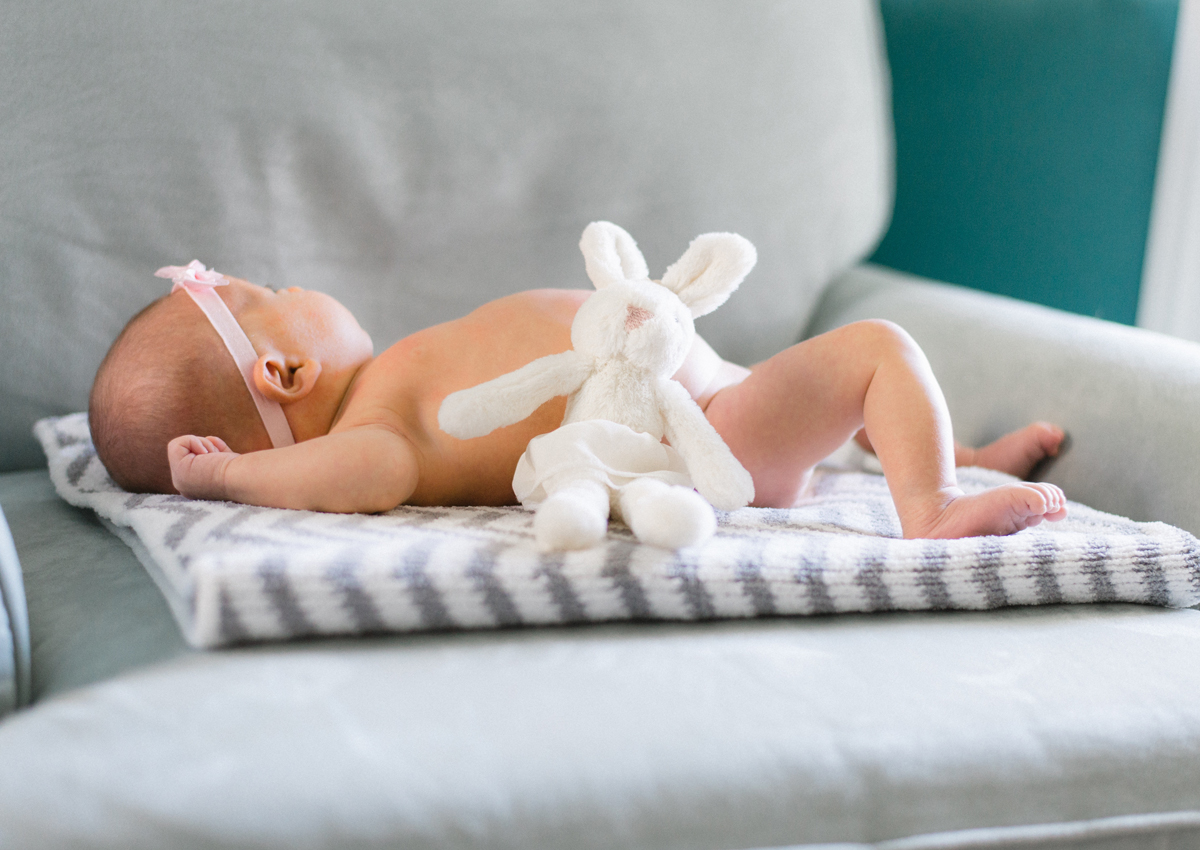 Pasgeboren baby met een witte knuffel op een grijze bank